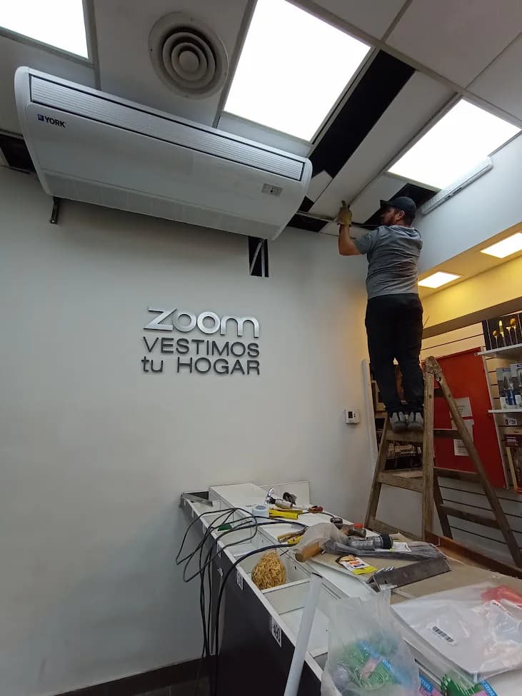 Técnico sobre una escalera trabajando en un equipo de aire acondicionado dentro de un comercio.