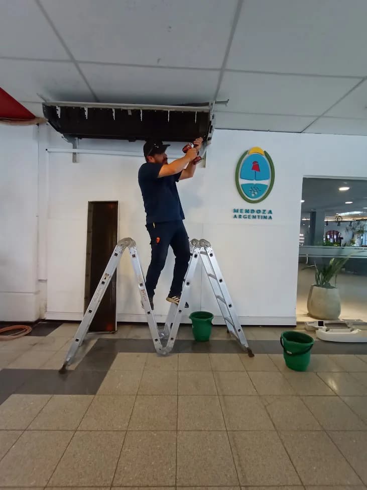 Técnico sobre una escalera trabajando en un equipo de climatización instalado cerca del cielorraso.